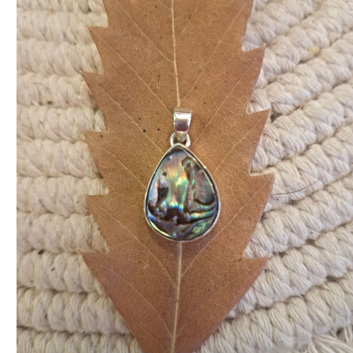 Close-up of iridescent abalone shell teardrop pendant in silver bezel
